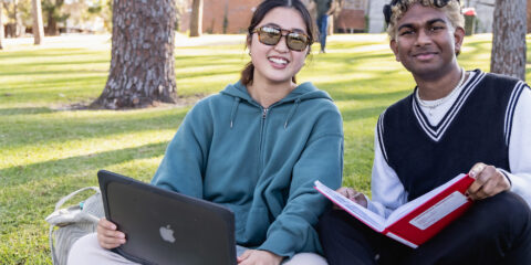 A male and female student sitting on grass and smiling