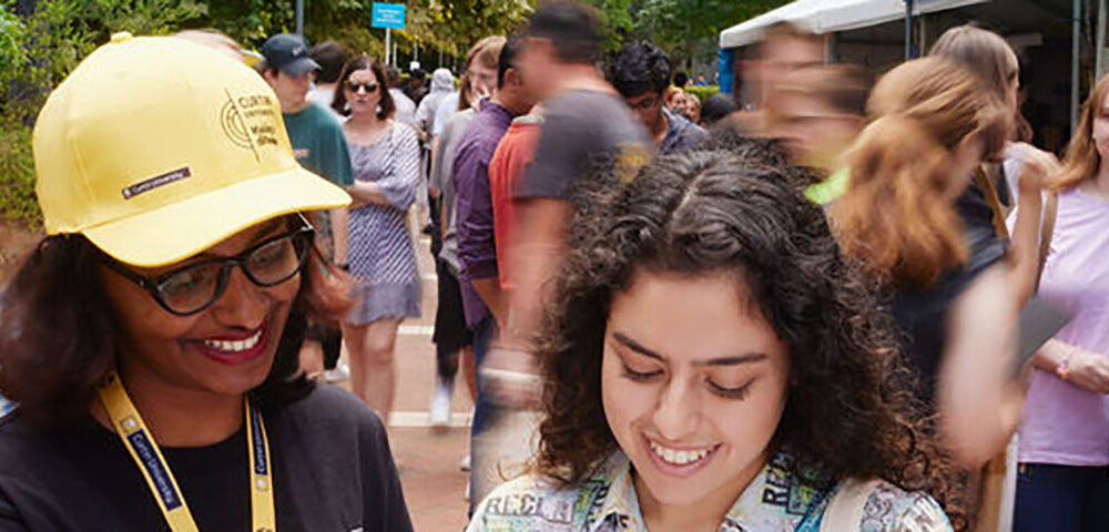 2 Students looking at a book amidst a crowd.