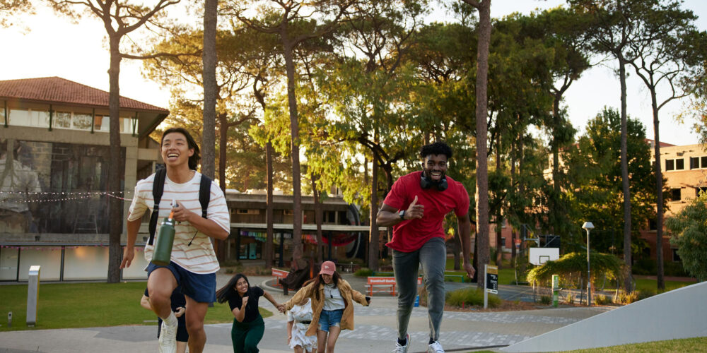 Students running on Curtain campus, laughing