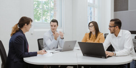 4 people in business attire sitting around a table and talking amongst themselves.