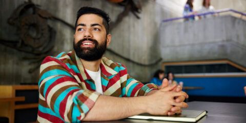 A student in a striped sweater sits at a table on campus smiling