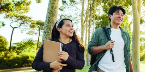 Three students laugh as they walk across campus in the sunshine