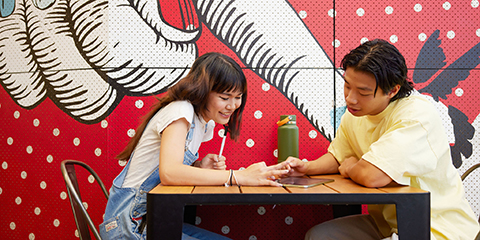 Two students helping eachother study on an ipad in a study space.