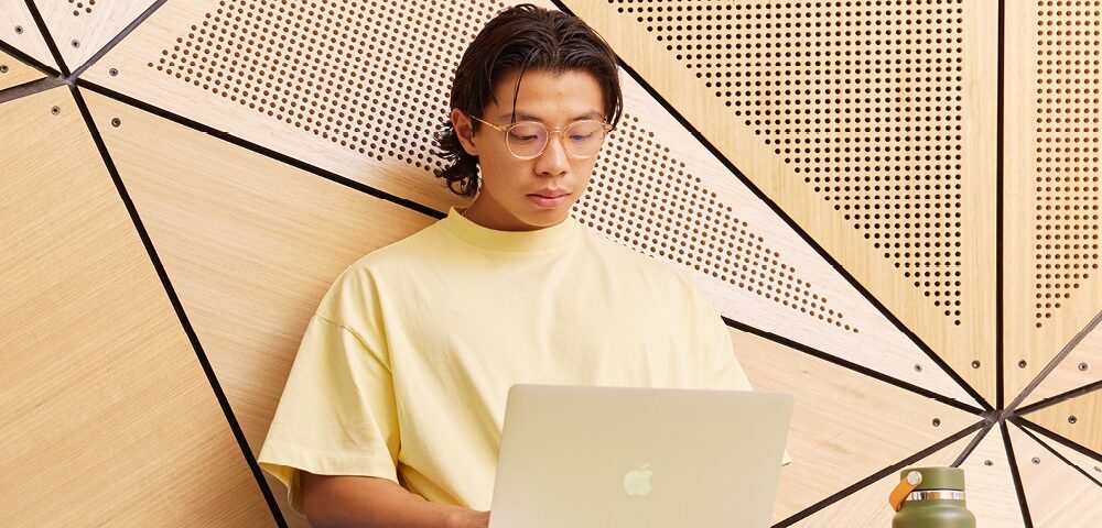 A student wearing a yellow t-shirt studies on a laptop