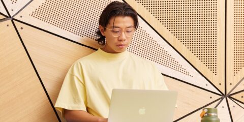 A student wearing a yellow t-shirt studies on a laptop