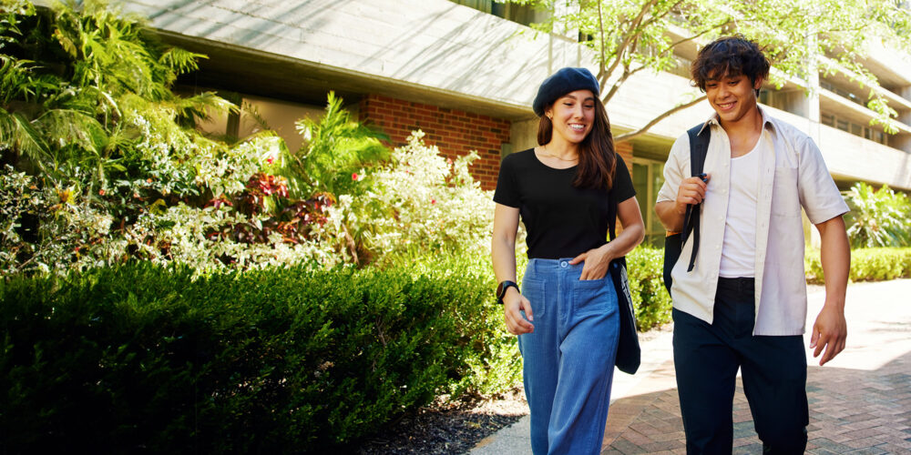 Two students walking through Curtin campus laughing.