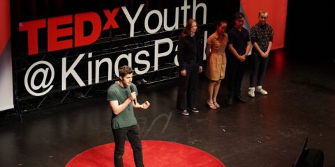 Person stands on stage talking at TEDx Youth Kinds Park