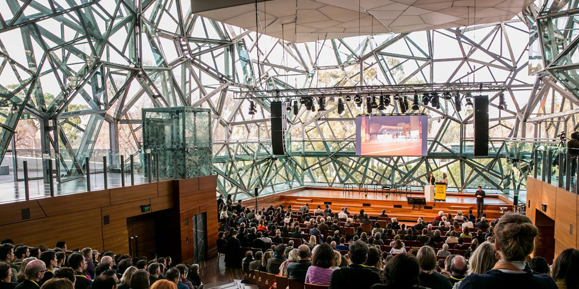 An image from a previous Living Cities forum where individuals are sitting in the crowd listening to keynote speakers.