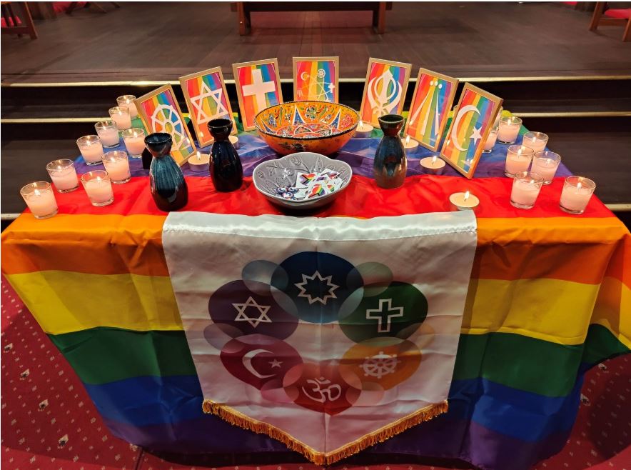 Table with rainbow flag and various religious symbols.