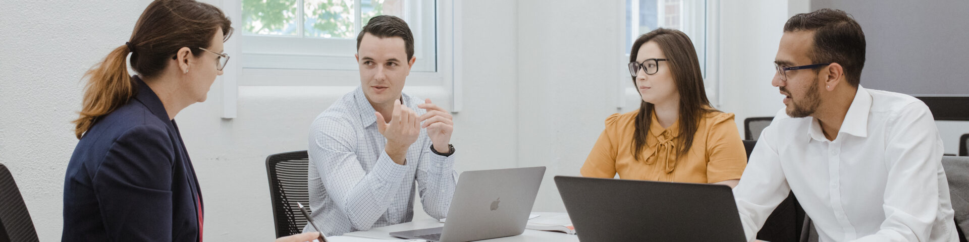 4 people in business attire sitting around a table and talking to each other.