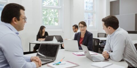 Four people dressed in business attire chat around a table