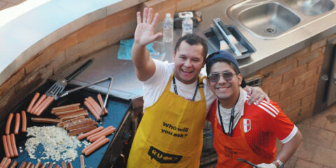 Two male Kalgoorlie students smiling and waving while cooking a barbecue.