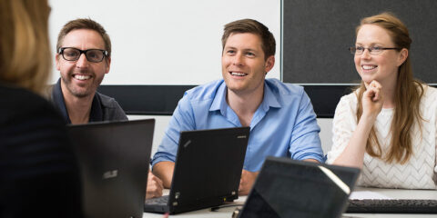 Three students smiling in a classroom.