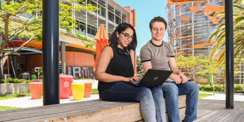 Two students sitting on a bench looking at a laptop.