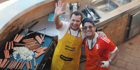 Two people waving while cooking sausages