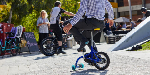 Person riding a small bike with training wheels at an outdoor event.