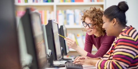 Two students pointing at monitor and discussing presentation on computer together during computer course at college