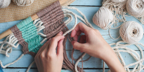 Hands weaving yarn and string on a table during a craft-based volunteering activity.
