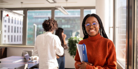 A female student carrying books and smiling at the camera