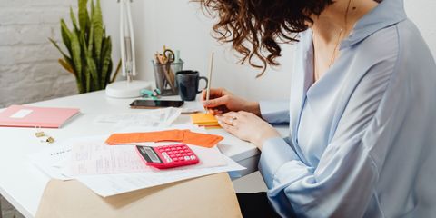 Woman writing with calculator on desk, managing finances indoors.
